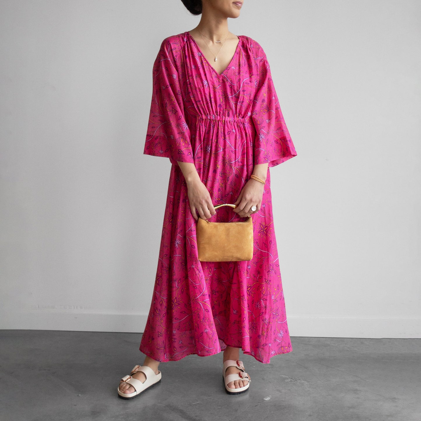 Floral print Angela Dress in Fuschia Melon, featuring a deep V-neck and bell sleeves, styled with a purse.