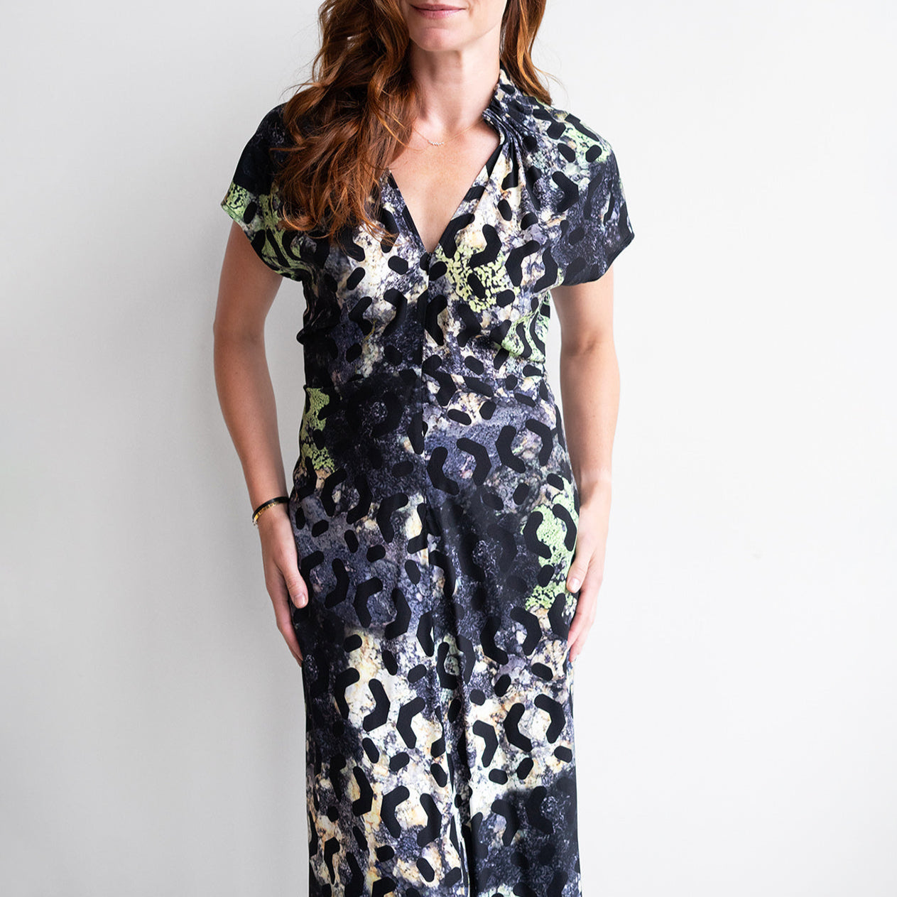 Woman wearing Stella Ruched Dress in Silk Moss, featuring V-neckline and gathered collar, showcasing vibrant print.