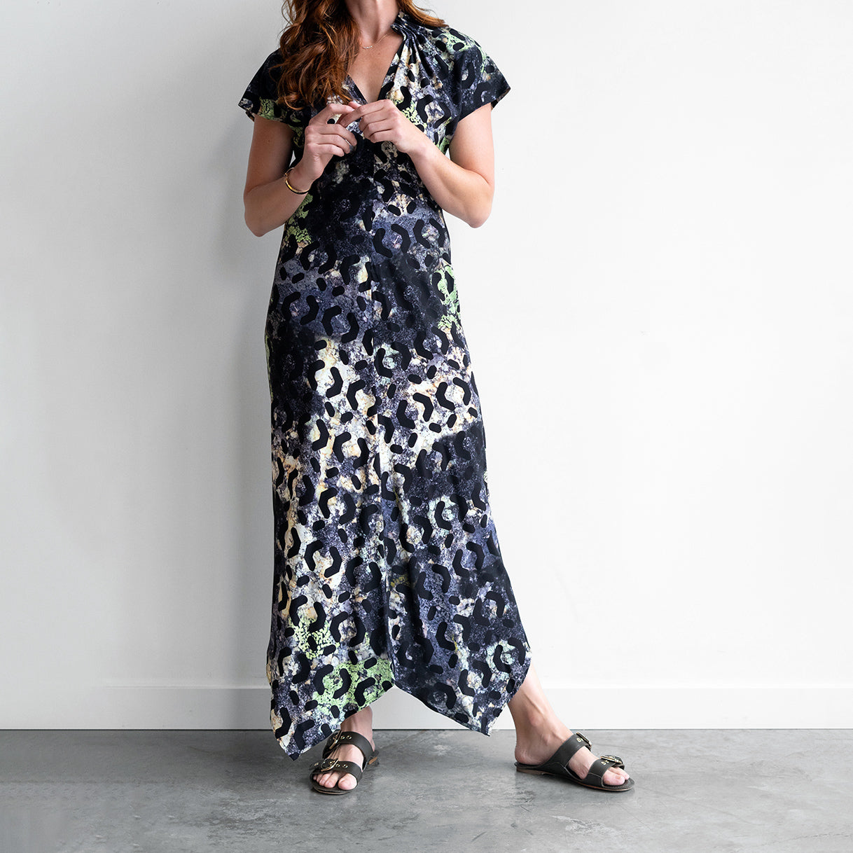 Stella Ruched Dress in Silk Moss, featuring a V-neckline and asymmetrical hem, styled with casual footwear.