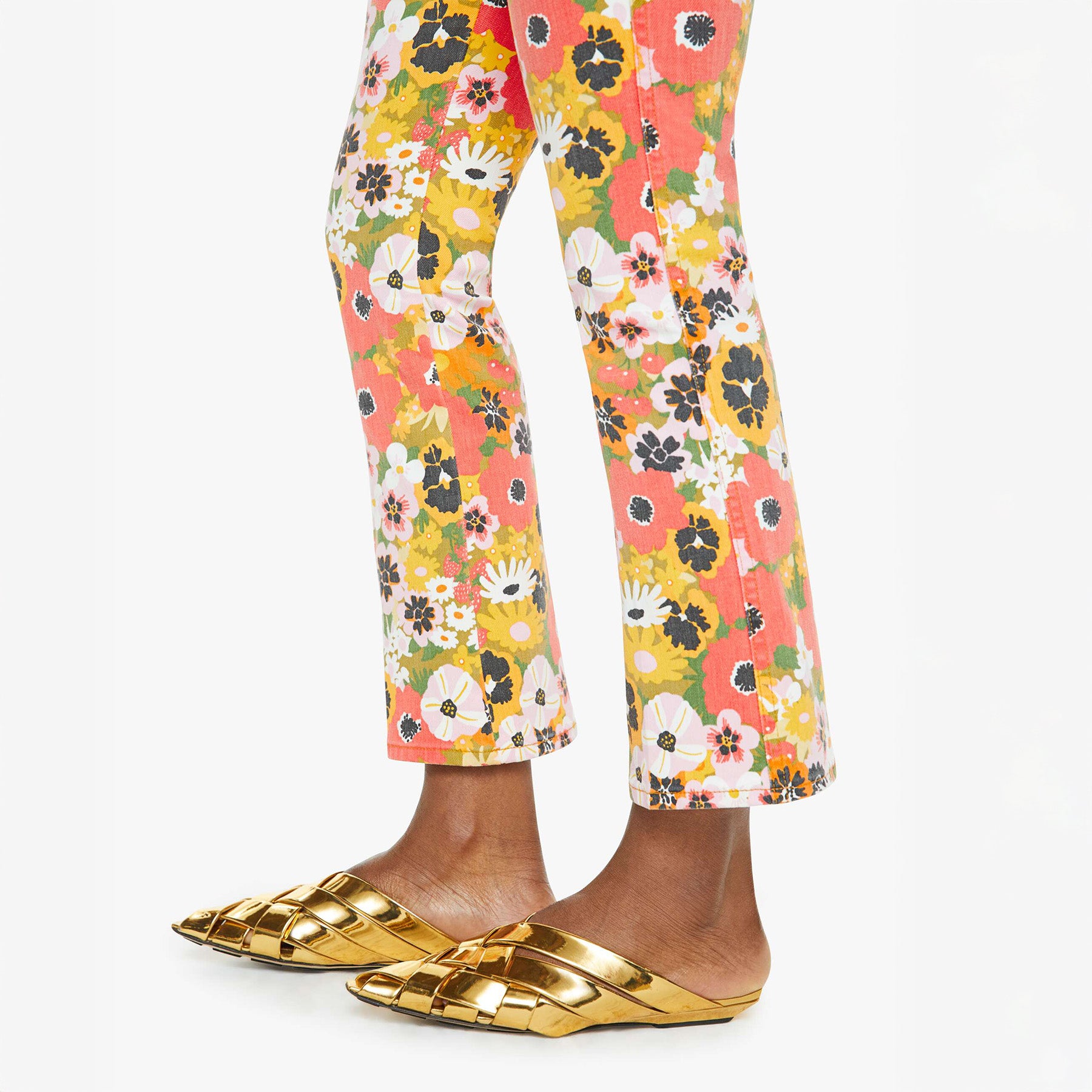 Mid-rise flared jeans in colorful floral print, paired with stylish gold mules, showcasing trendy summer fashion.