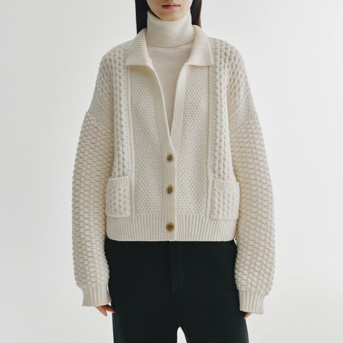 Becs Cardigan in Cream displayed on model, featuring a relaxed silhouette and cable knit design.