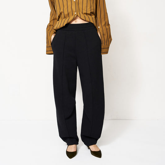 Pintuck Track Pant in Black displayed on model with a striped shirt, showcasing relaxed fit and pintuck details.