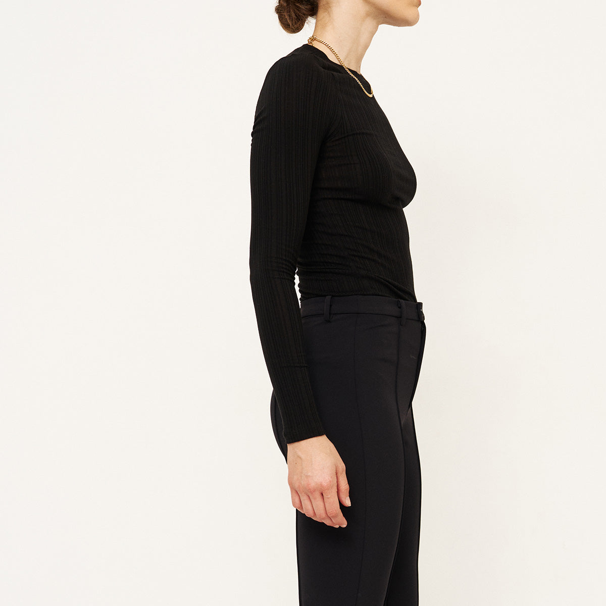 Side view of a woman wearing a Long Rib Tee in Black, showcasing the slim fit and ribbed texture.