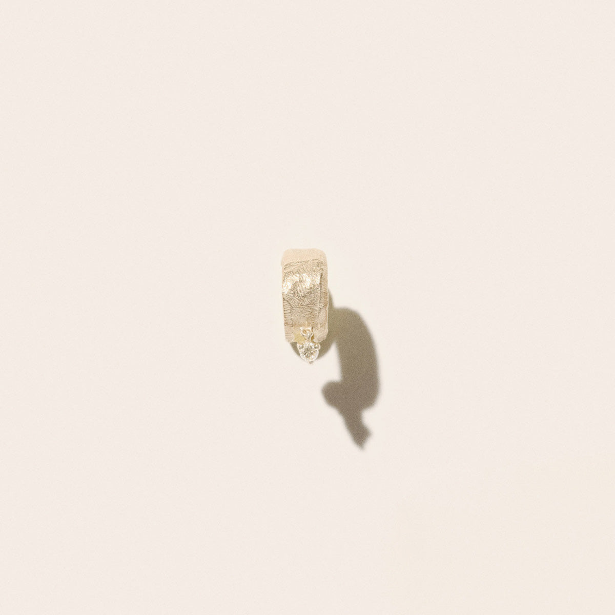 Gaby No.1 Earrings in 9K Yellow Gold textured hoop earring with suspended diamond on a light background.