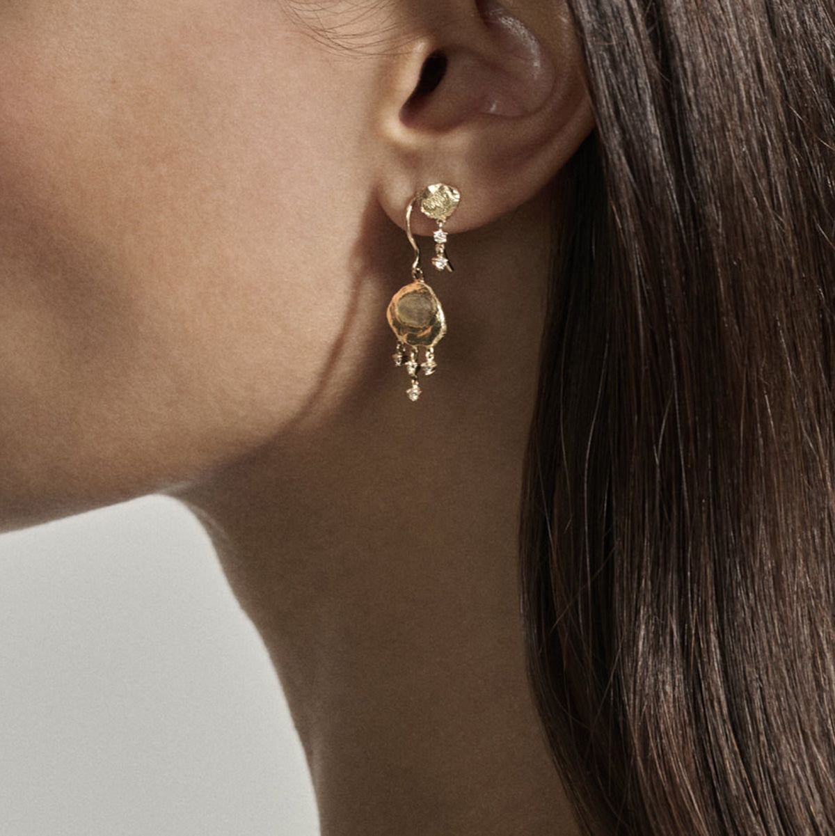 Marla No. 1 Earrings in 9K Yellow Gold displayed in a model's ear with small suspended diamonds and hammered design.