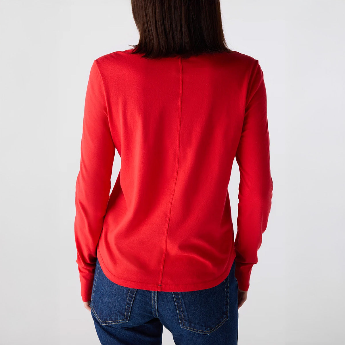 Back view of a woman wearing the Quinn Longsleeve Tee in Signal, showcasing curved hem and back center seam in vibrant red.