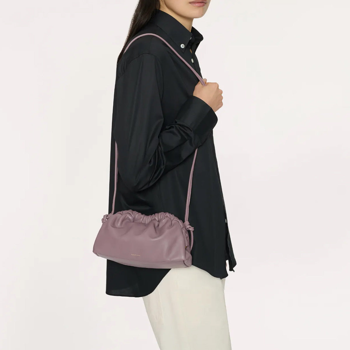 Woman holding a Mini Cloud Clutch in Uva, a sculptural leather bag with a curved frame and detachable strap.
